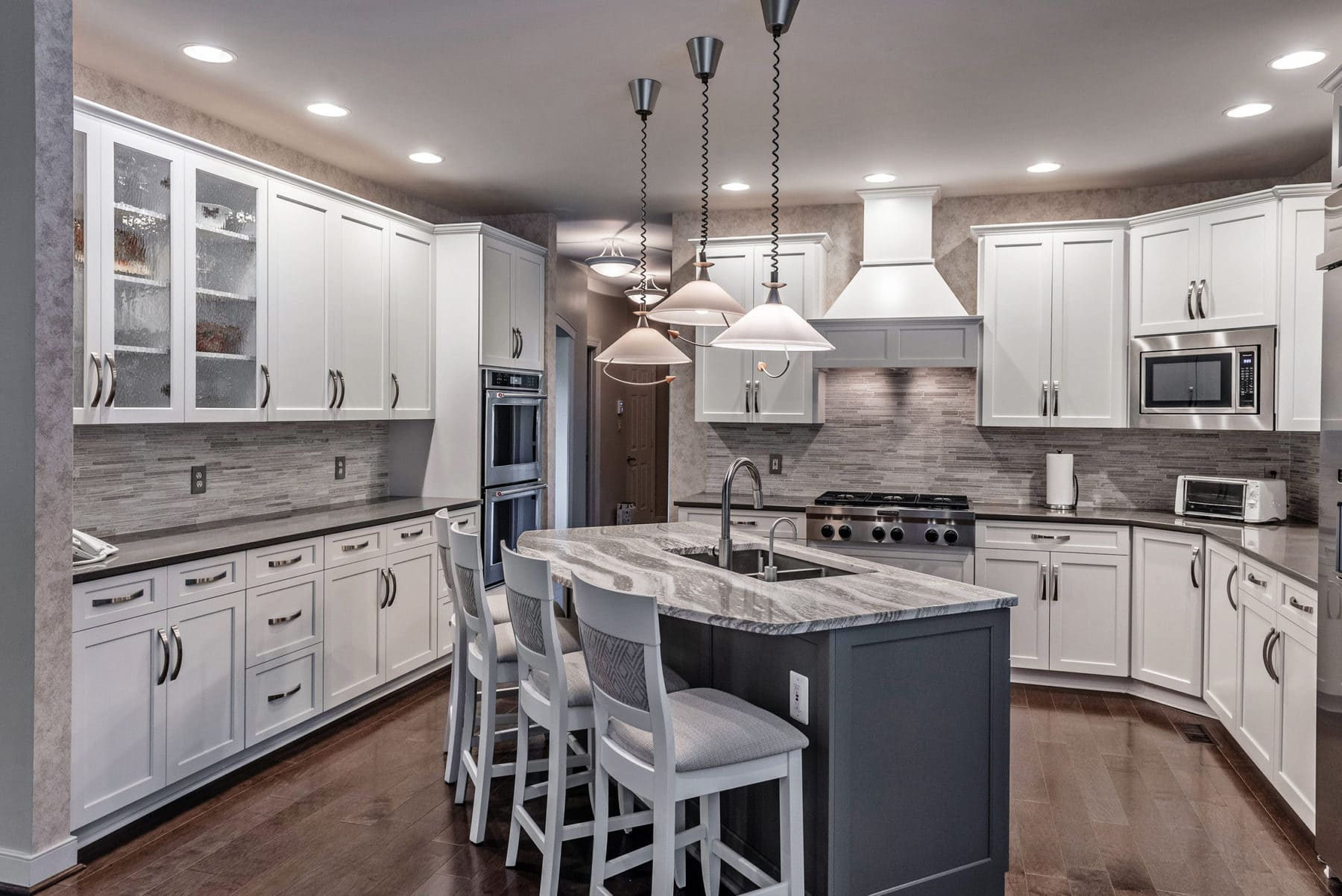 A gray and white kitchen with quartz countertops and stainless-steel appliances.