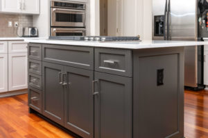 White overhead cabinets in a kitchen with a kitchen island featuring grey cabinets under the countertop.