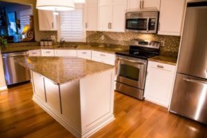 A newly renovated kitchen with white cabinetry, marble countertops, wood flooring, and under-cabinet lighting 