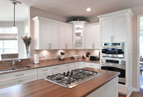 A wooden butcherblock countertop finished with a dark brown stain in a kitchen with white cabinets.