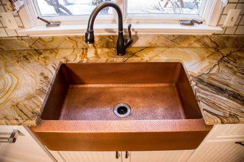 Painted cabinets and textured copper make a bold statement in this refaced kitchen. The eyecatching and formal 16 gauge copper range hood is balanced by the smooth color and rustic detail of the LaFayette cabinet doors. Likewise, a valance and apron sink add a lot of character to the design, while a hidden trash/recycling pullout adds convenience.