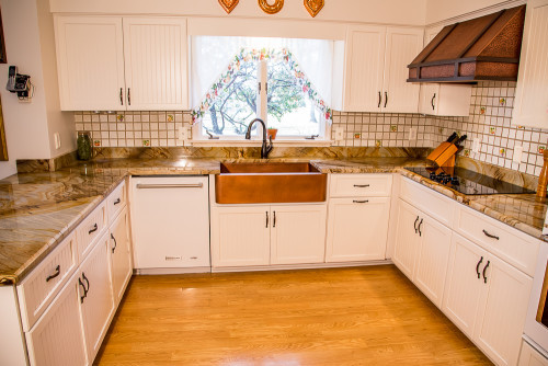 Painted cabinets and textured copper make a bold statement in this refaced kitchen. The eyecatching and formal 16 gauge copper range hood is balanced by the smooth color and rustic detail of the LaFayette cabinet doors. Likewise, a valance and apron sink add a lot of character to the design, while a hidden trash/recycling pullout adds convenience.