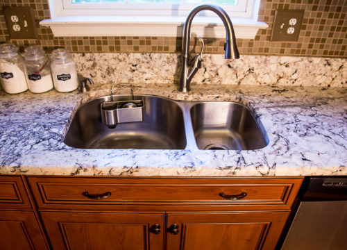 This kitchen was expanded and refaced in a warm wood-look laminate, and looks great! Existing cabinets were refaced and repaired, and new cabinets were added along with the new exteriors. Two of the kitchen cabinets received storage upgrades with full extension rollouts, while another got a pull out base organizer and a tip out tray added storage to the sink area. A classy and custom look was created by adding details like a mullion glass door, crown molding, a light rail and base molding.