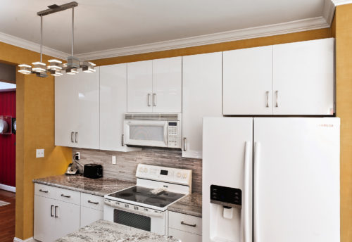 This kitchen went from rustic to recent with an update by Kitchen Saver. These shaker-styled laminate doors and long bar style handles create a look that’s firmly contemporary, while details like the range hood and wood grain patterns keep a sense of warmth in the design. Two appliance garages keep necessary tools close at hand without cluttering the counter.