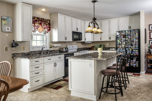 This kitchen was refaced with white laminate in a classic design. A glaze on the doors highlights the details of the design, and crown moulding adds a finished look to the room. A lazy susan allows the full space of a corner cabinet to be easy to access storage.