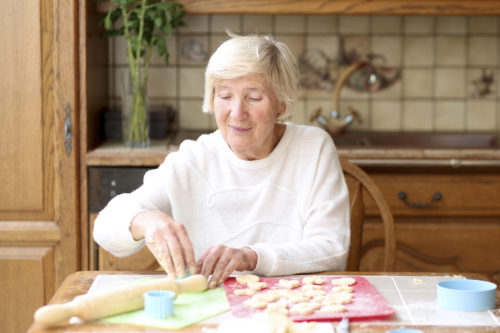  Older person sitting at a table to work on a spread of cutout cookies