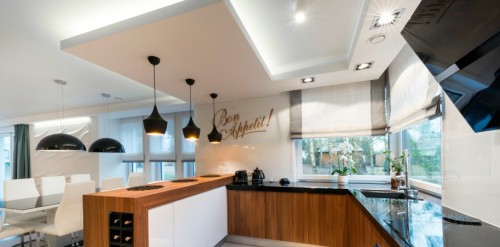 Modern kitchen interior design in black and white style, showign pundants, ambient lights, and recessed task lighting.